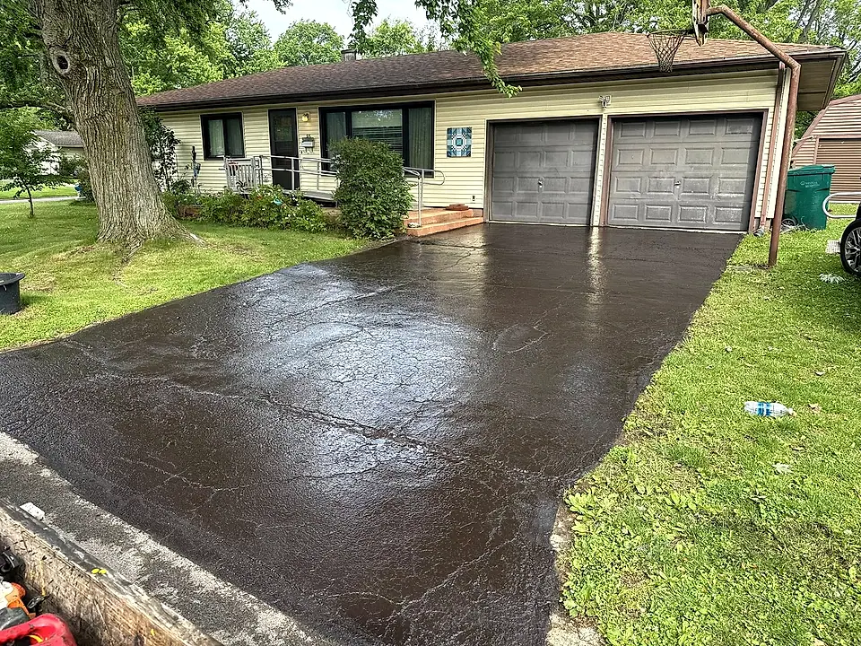 Ranch-home driveway freshly seal-coated to a deep wet-black finish