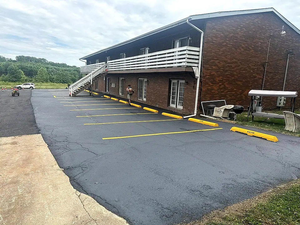 Freshly sealed parking lot beside a brick building with new yellow stalls and speed bumps