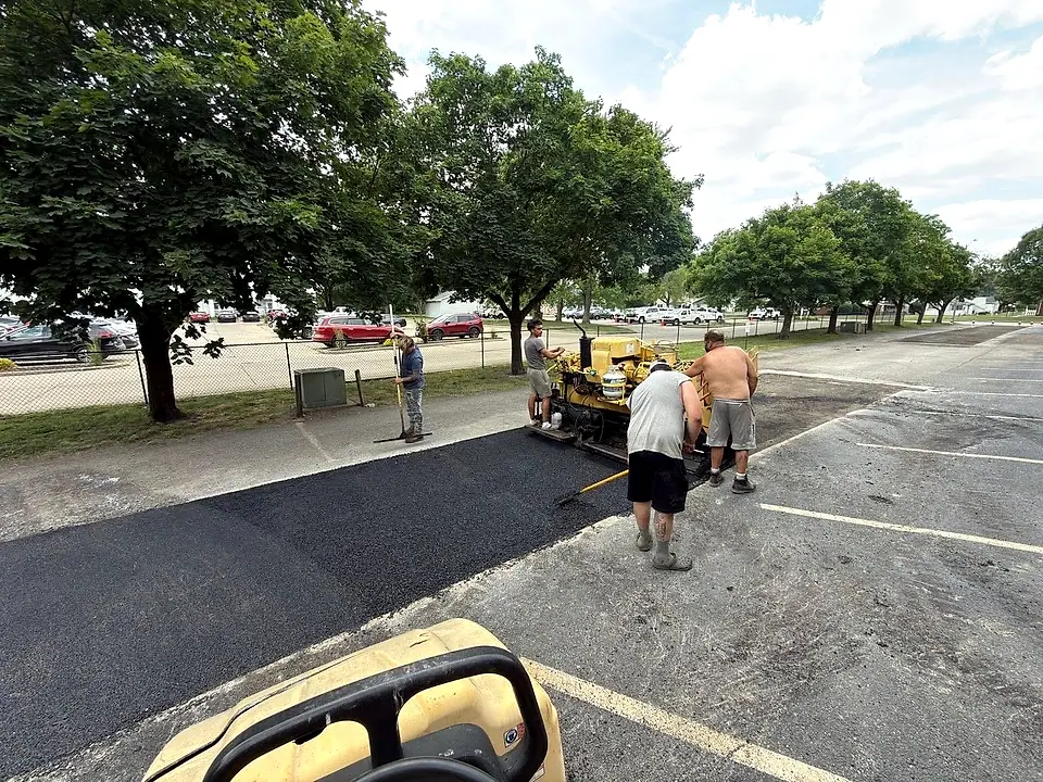 Crew laying fresh asphalt with the paver machine on a parking lot