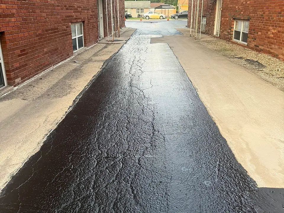 Glossy freshly sealed asphalt path running between two brick buildings
