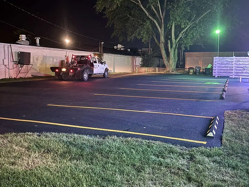 Fresh yellow striping and speed bumps on a sealed lot at night with the work truck